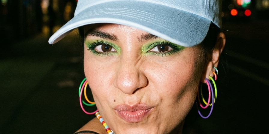 Woman wearing a light blue embroidered dad cap reading “Accepto disculpas en efectivo” at night.