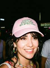 Woman wearing a pink embroidered dad cap reading “Accepto disculpas en efectivo” at night.