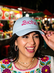 Woman wearing a light blue embroidered dad cap reading “Bicha” during a nighttime outing.