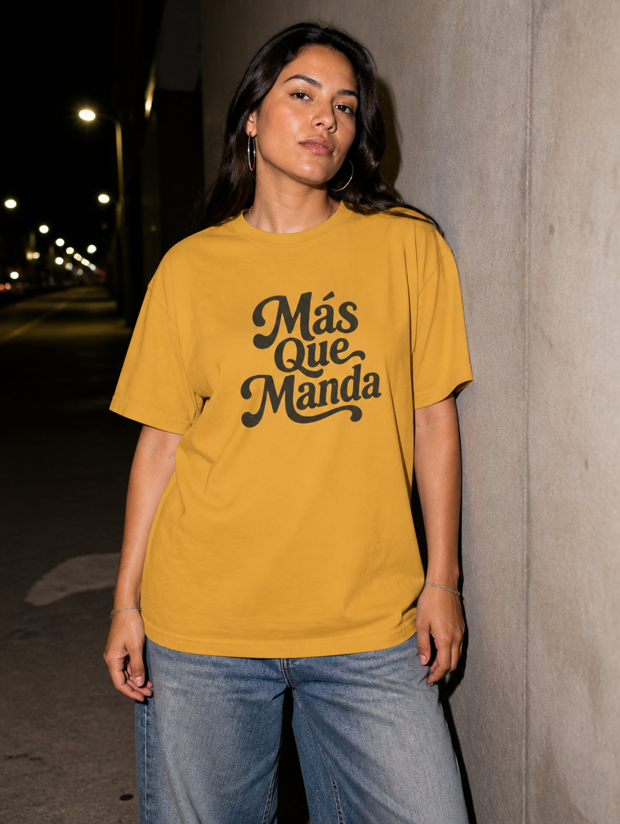 Latina model wearing the Más Que Manda T-Shirt in Faded Mustard at night