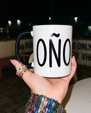 Close-up of a hand holding a white and black “Coño” mug during a nighttime outing.