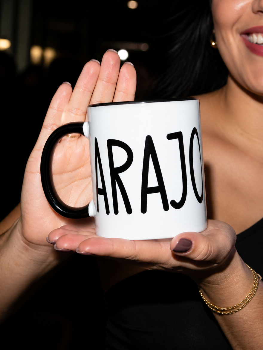 Woman holding a white mug with black interior and handle featuring “Carajo” in tall black lettering at night.