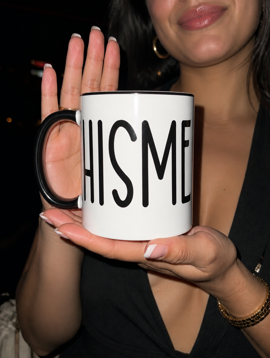 Woman holding a white mug with black interior and handle featuring “Chisme” in tall black lettering at night.
