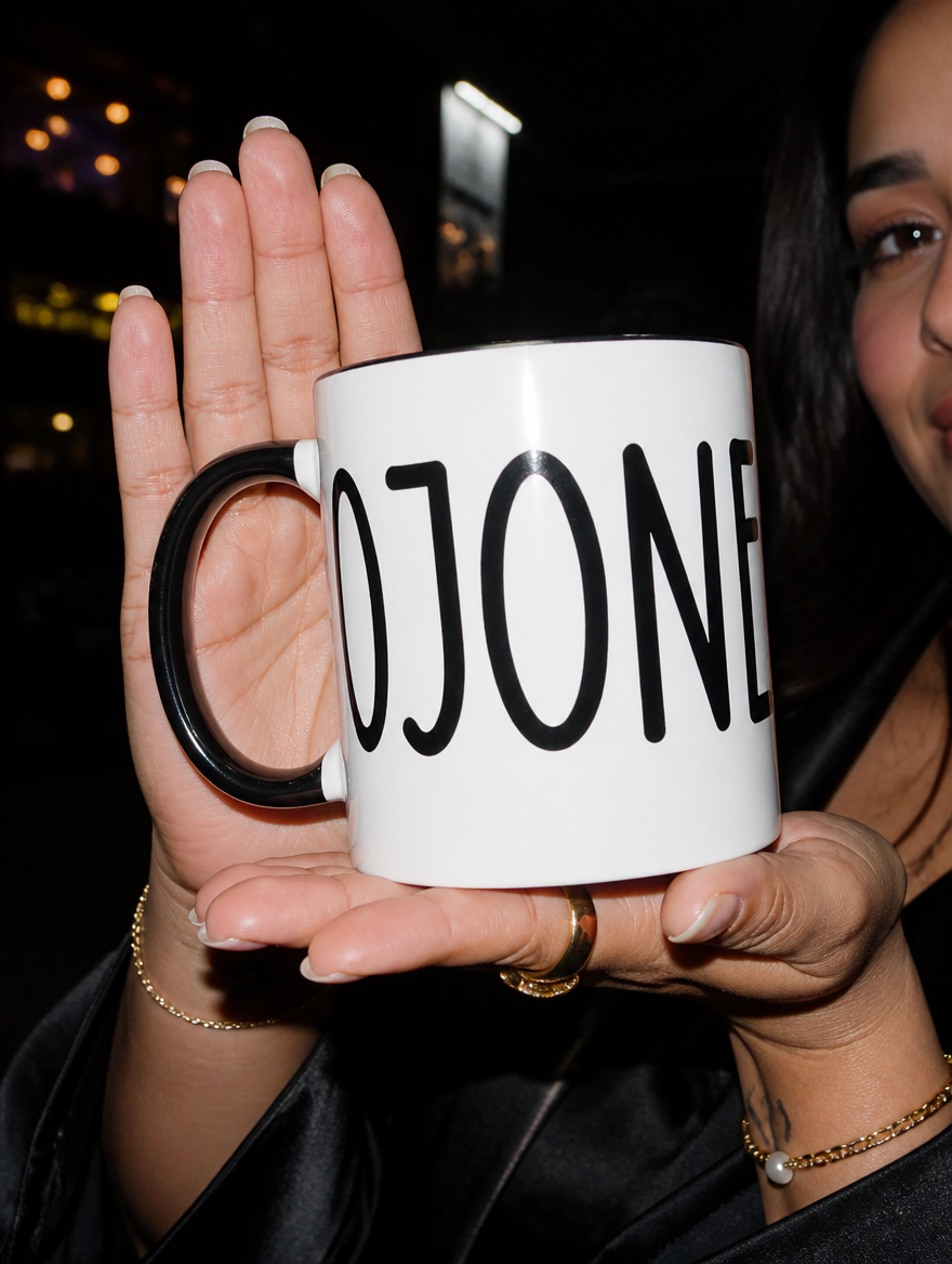 Close-up of a woman presenting a white and black “Cojones” mug during a nighttime outing.