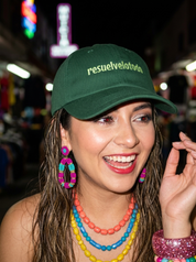 Woman wearing a dark green embroidered dad cap reading “resuelvelotodo” during a nighttime outing.