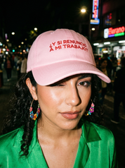 Woman wearing a pink embroidered dad cap reading “¿Y si renuncio a mi trabajo?” at night.